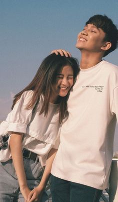 a man and woman standing next to each other near the ocean with their arms around each other