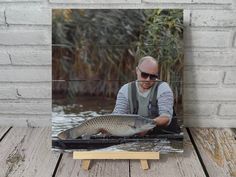 a man holding a large fish on top of a wooden table next to a brick wall