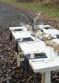 an outdoor table set with place settings and candles on it, in the middle of leaves