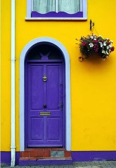 a purple door and window on a yellow building with flowers in the window sill