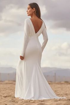 a woman standing on top of a sandy beach wearing a white dress and long sleeves