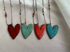 three heart shaped necklaces hanging from strings on a white cloth background with beaded cord