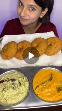 a woman holding up three trays of food with different dips and sauces in front of her