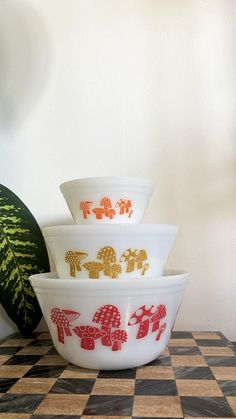 four bowls with elephants painted on them sitting on a checkered counter top next to a plant