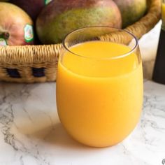 a glass of orange juice next to a basket of mangoes and pears on a table