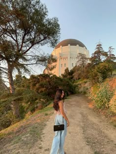 a woman standing on a dirt road in front of a large building with a dome