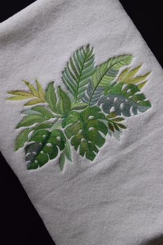 a white towel with green leaves embroidered on the front and back of it's edges