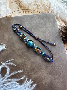 a blue beaded bracelet with pearls and beads on a gray cloth next to feathers