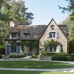 a stone house with blue shutters and ivy growing on the windows is surrounded by lush green grass