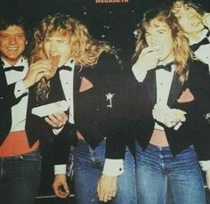 four people dressed in tuxedos posing for a photo with one woman biting into the other's mouth