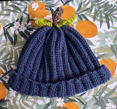 a blue knitted hat with a green bow on the top and two small crochet bows at the end