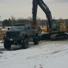 a large truck is parked in the snow with a construction vehicle behind it and a bulldozer