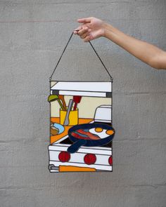 a hand holding up a stained glass sign with an oven and kitchen items on it