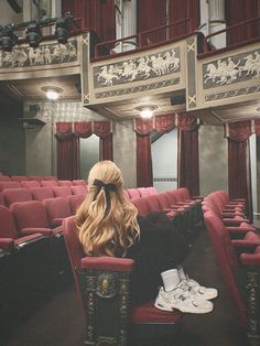 a woman sitting in a red chair with her back to the camera, facing an empty theater