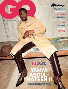 a man sitting on top of a wooden bench wearing a trench coat and brown pants