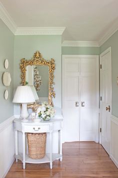 a white table topped with a lamp next to a mirror and a basket filled with flowers