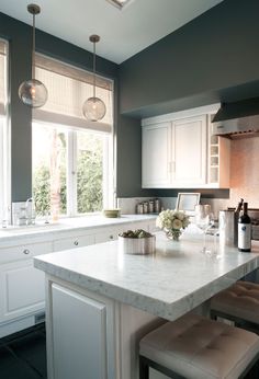 a kitchen with white cabinets and marble counter tops in front of a large open window