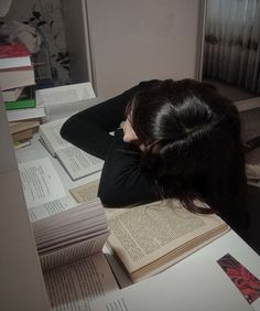 a woman sitting at a desk with books on it and her head in her hands