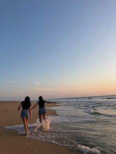 two women walking on the beach with their hands in each other's pockets as the sun sets