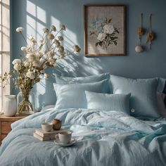 a bed with blue sheets and white flowers in a vase on the end table next to it