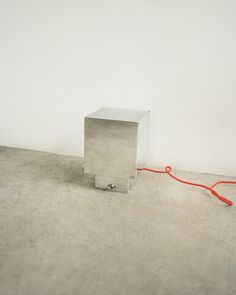 a square object sitting on the ground next to a red cord that is connected to it