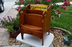 a wooden chair sitting on top of a white pedestal next to flowers and a potted plant