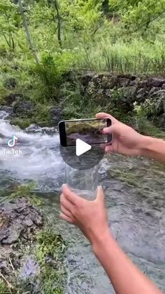 someone is holding up their cell phone to take a photo of a stream in the woods