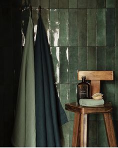 a wooden stool sitting next to a green tiled bathroom wall with a bottle of shampoo on it