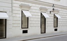 an empty street in front of a white brick building with windows and awnings