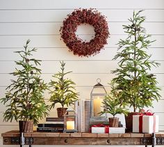 christmas trees and presents on a table in front of a white wall with a wreath