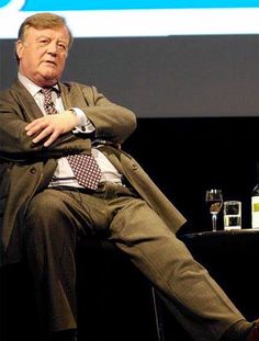 an older man sitting on a chair in front of a screen with his feet crossed