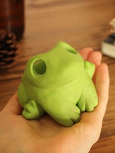 a hand holding a green toy frog on top of a wooden table