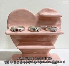 three rings are sitting on top of a pink heart shaped display stand with the words love written in korean