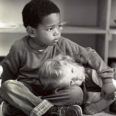 two children sitting on the floor playing with each other and looking at something off to the side