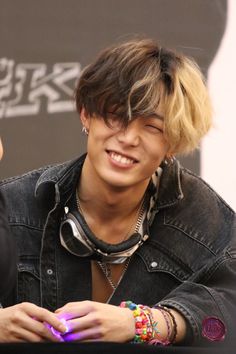 a young man with blonde hair and piercings smiles while holding a cell phone in his hand