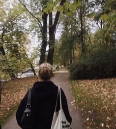 a woman walking down a leaf covered path carrying a white bag with the words no motion on it