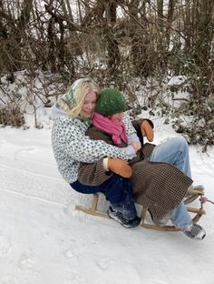 two people sitting on a sled in the snow, one holding onto the other