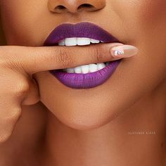 a woman with purple lipstick and white nails holding her finger up to her lips while looking at the camera