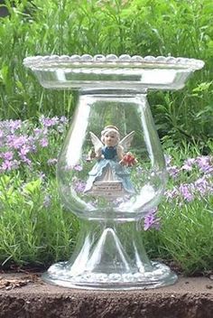 a glass vase with a fairy sitting on top of it next to purple flowers and grass