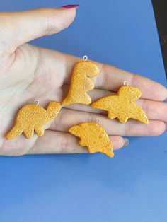 four yellow dinosaur shaped earrings are shown on someone's hand with their fingers in the air