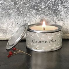 a candle is sitting in a tin next to some berries on the ground and snowflakes