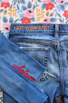 two pairs of jeans with the words not your baby written on them, next to a floral wallpaper