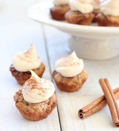 cinnamon rolls with icing and cinnamon sticks on a white table next to a bowl of cinnamons