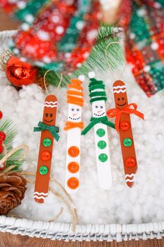 three snowman pops are sitting in the snow next to pine cones and christmas decorations