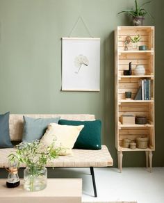 a living room with green walls and white carpeted flooring, a beige sofa is next to a bookcase filled with books