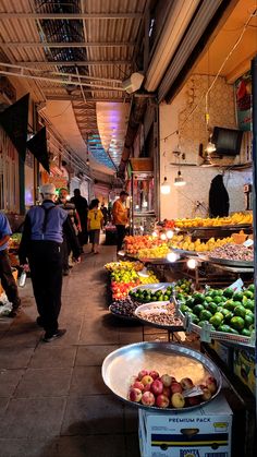 people walking through an open market with lots of fruits and veggies on display