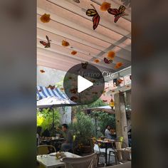 an outdoor restaurant with butterflies hanging from the ceiling and people sitting at tables under umbrellas