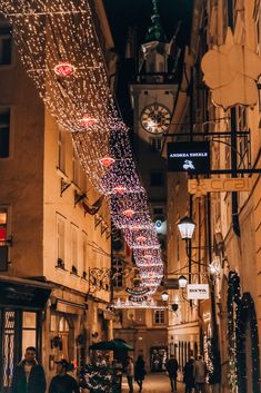 people walking down an alley with christmas lights on the buildings and clock tower in the background