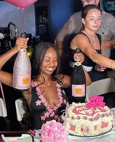 two women holding up bottles in front of a cake with pink frosting on it