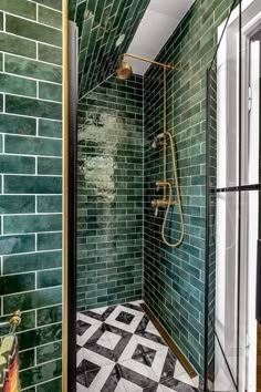 a green tiled bathroom with black and white floor tiles, shower head, and hand held shower faucet